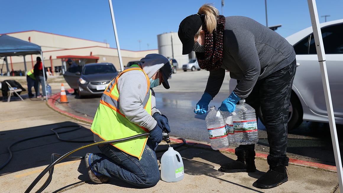 Volunteers fill water jugs for people at a drive-through water distribution center
