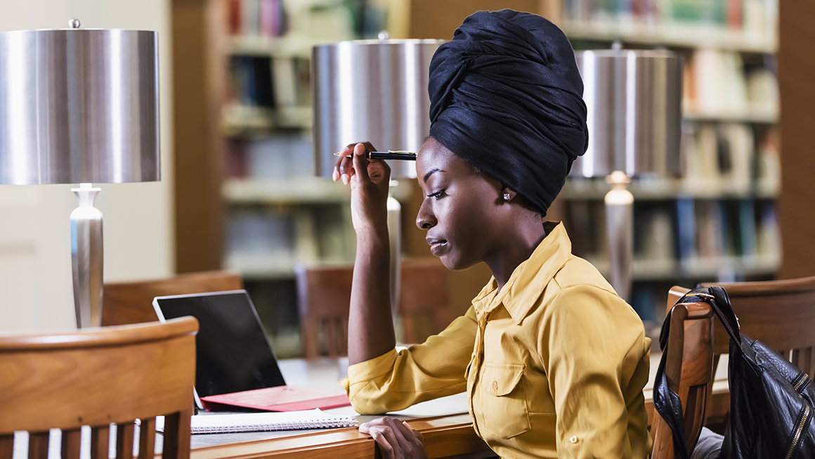 A young woman working at a desk in a library.