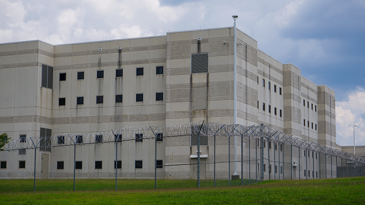 A modern correction facility surrounded by a fence and razor wire.