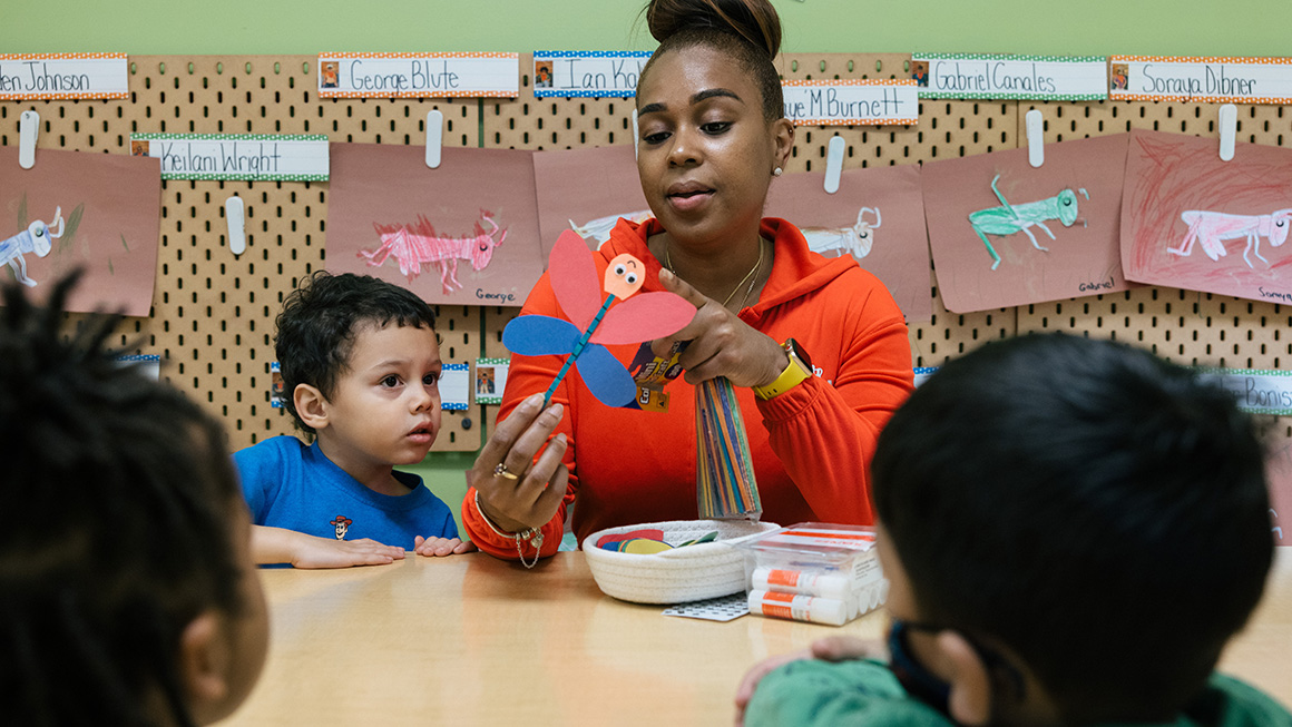A woman crafting with young children in a classroom.