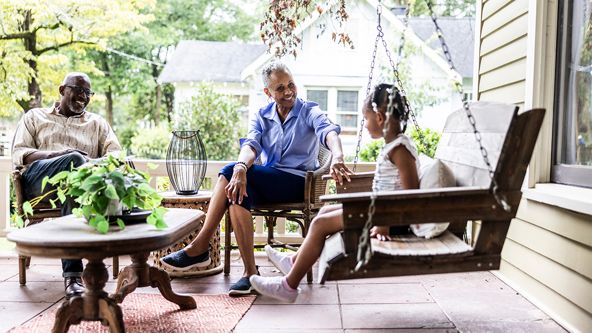 A grandfather, grandmother, and granddaughter sit on a front porch