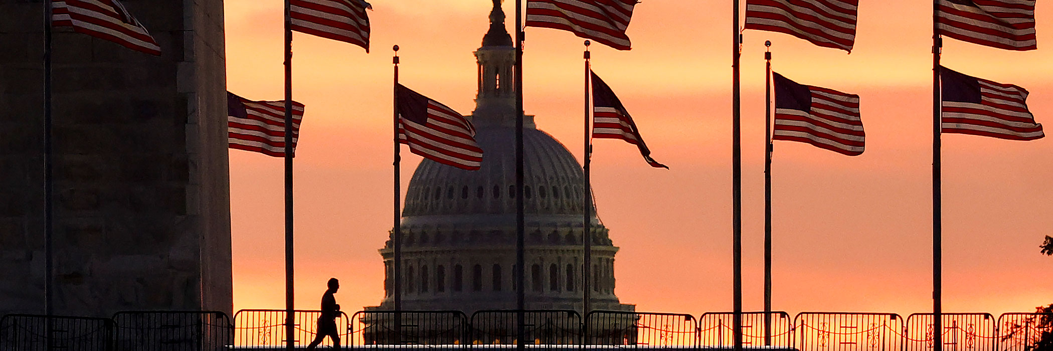 A person walking in front of the US capitol and American flags as the sun sets.