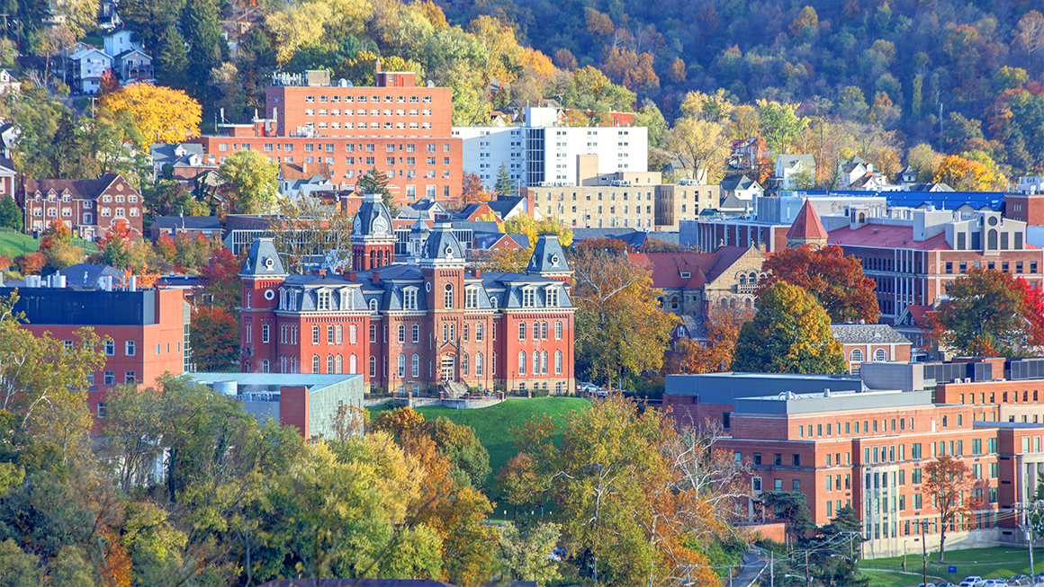 Photo of the University of West Virginia, with autumn foliage on the surrounding hills.