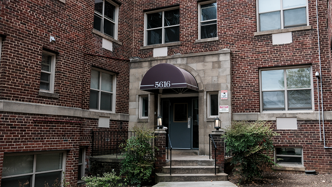 Brick apartment building entrance with steps, railing, shrubs, and awning labeled “5616.”