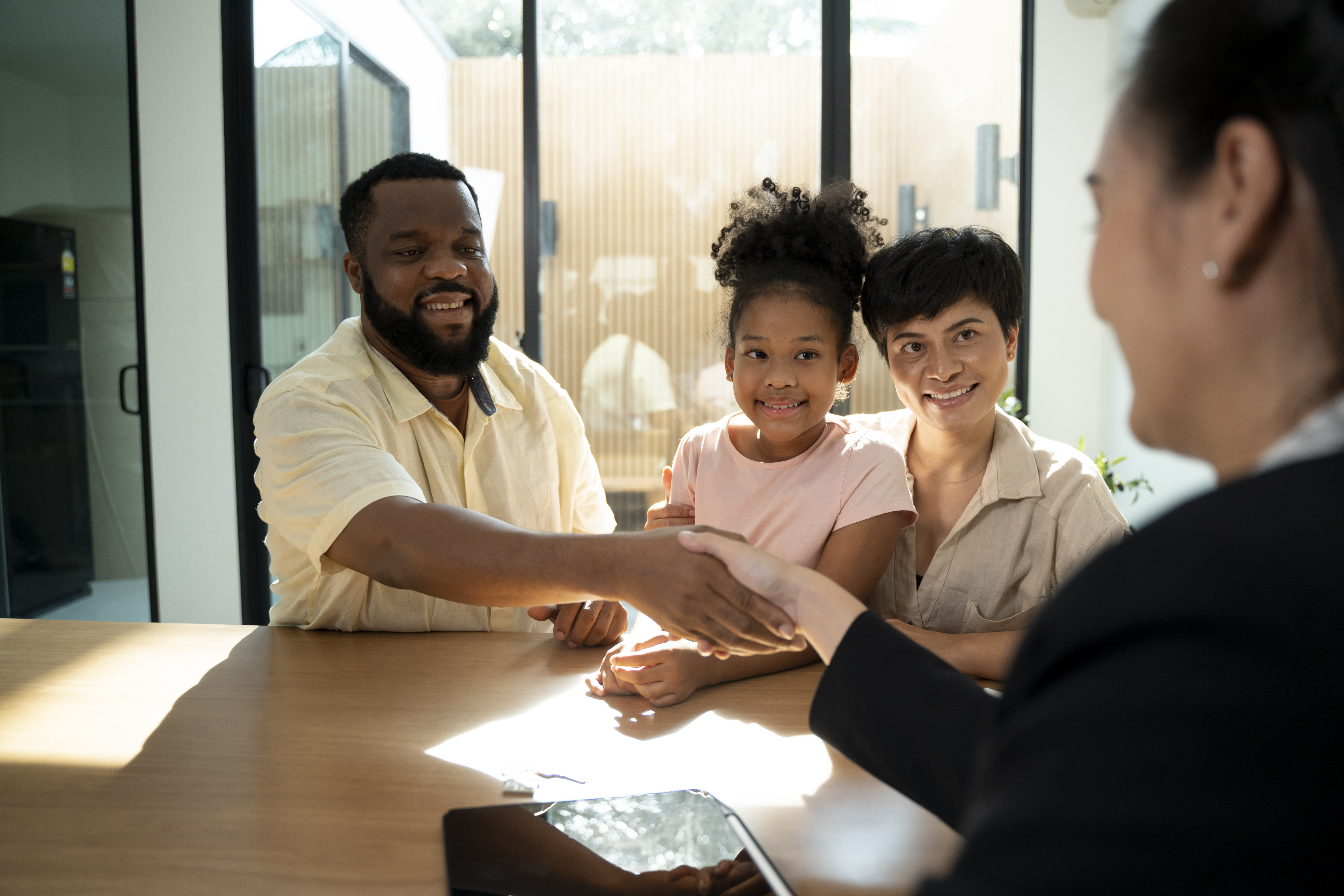 Person seated at a table shakes hands with a representative while two other people sit beside them in a bright office.