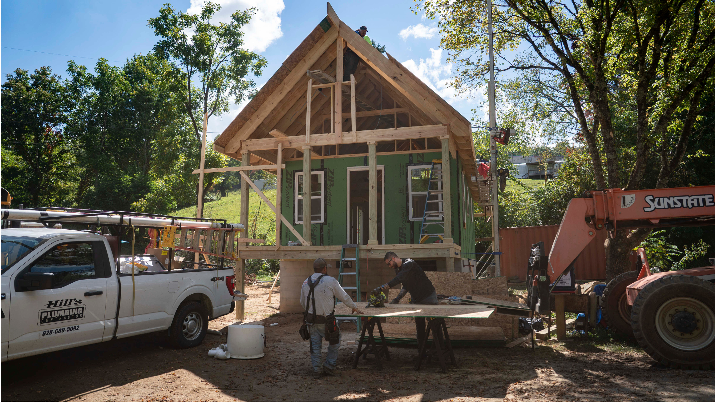 Workers constructing a small house during framing and exterior installation.