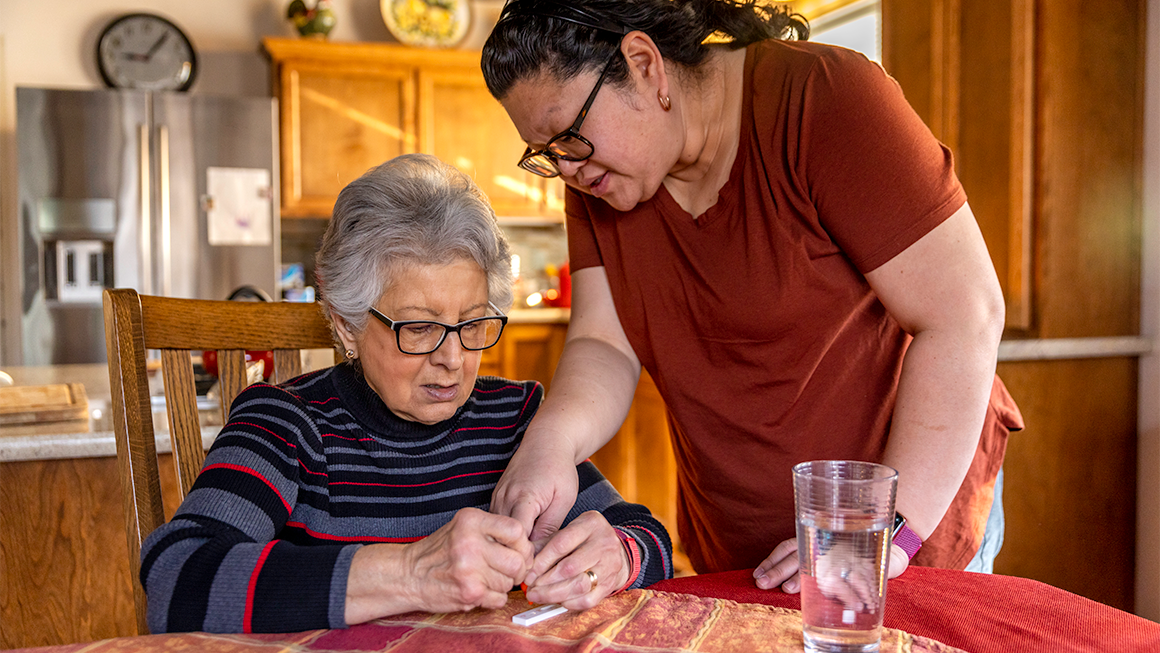 Photo of a direct care worker helping an older woman take a COVID test in her home. 
