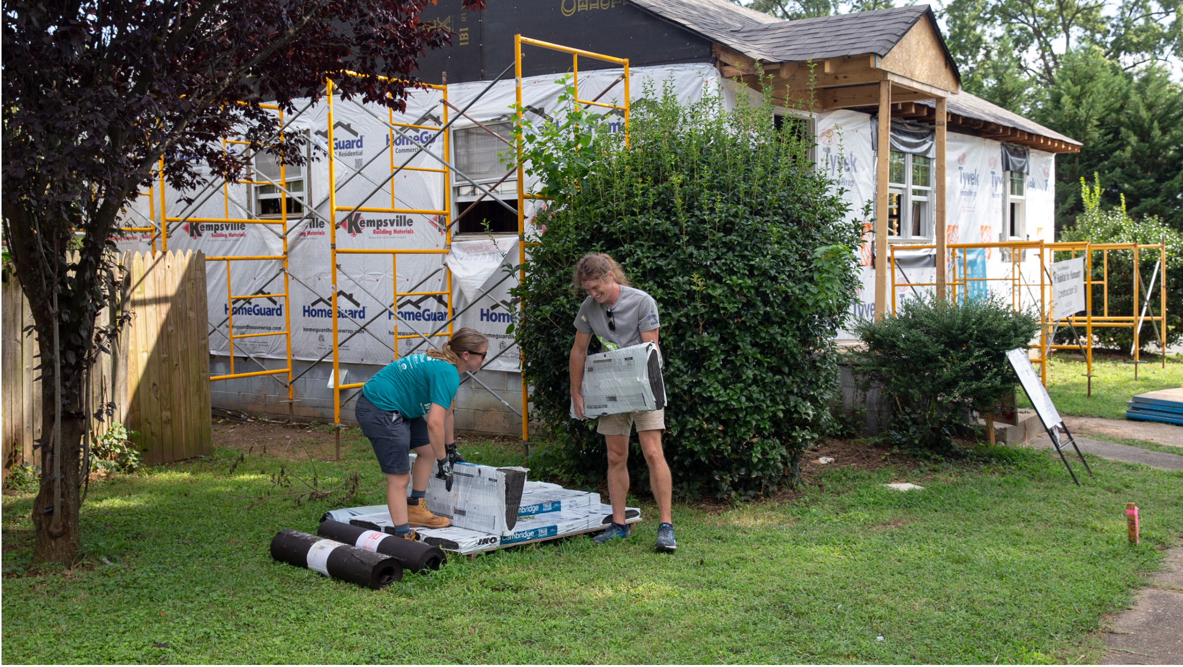 Volunteers carry construction materials in front of a house under renovation.