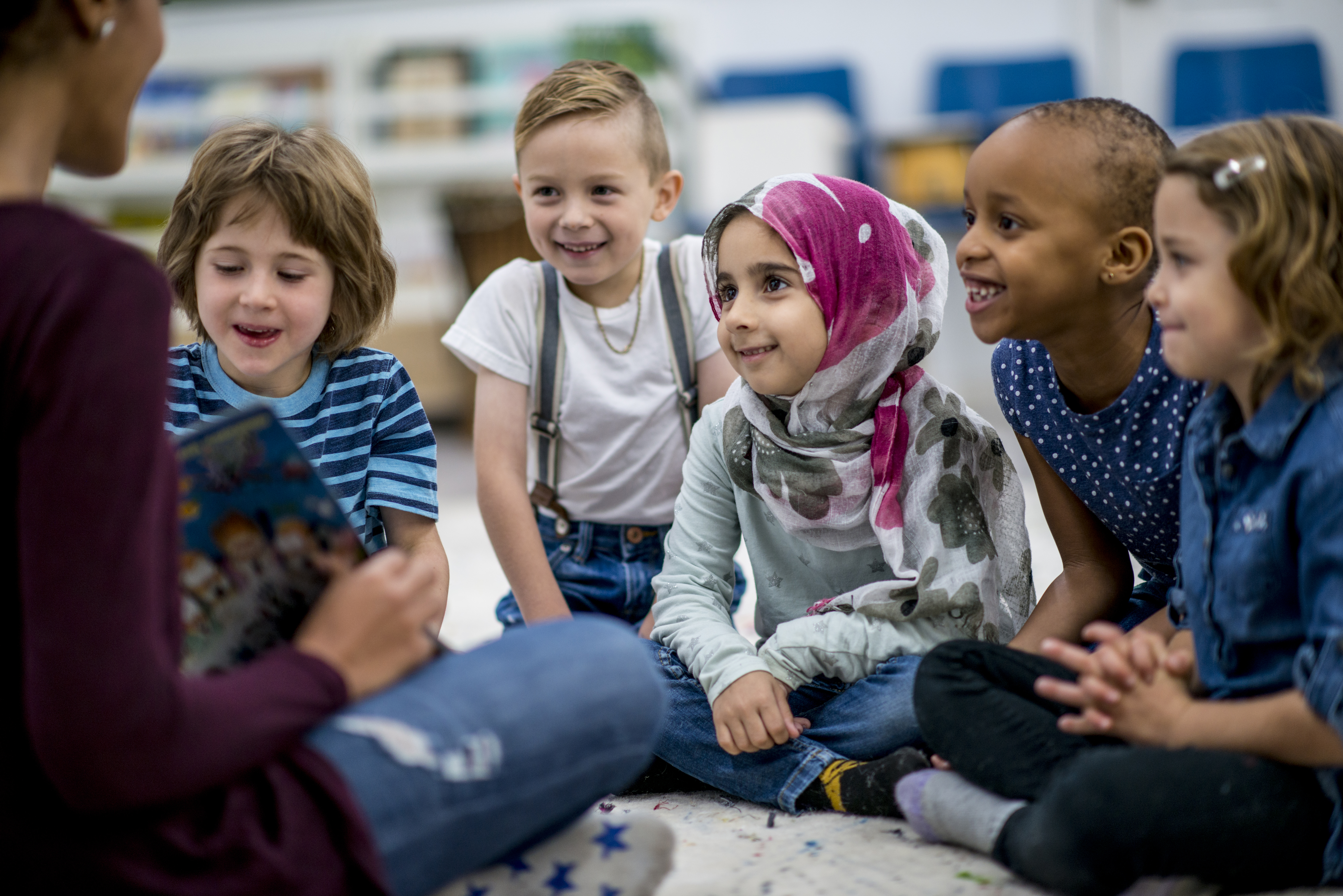 A multi-ethnic group of school children sitting on the floor and eagerly listening to their teacher read a storybook.