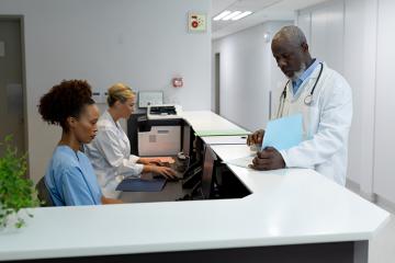Male and female doctors in hospital reception using computers looking at documentation