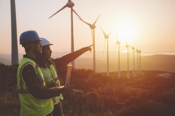 Young electrical engineer woman and business man standing in front of wind turbines