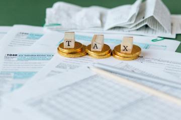 The word tax spelled out in blocks with each letter stacked on two coins. Also, a pile of tax forms.