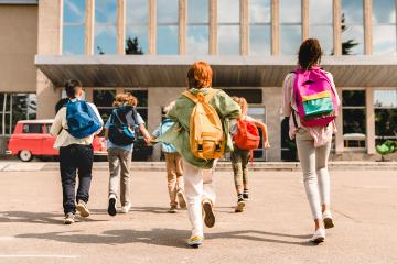 little school children wearing backpacks running into school
