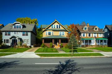 A streetview of three colorful multistory family homes on a sunny residential street.
