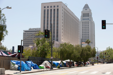 Many tents and makeshift shelters line a sidewalk in an urban setting.