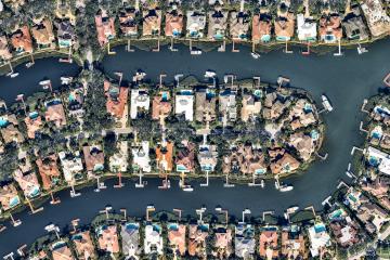 An aerial shot of what I swear is my big sister's neighborhood in South Florida, featuring large homes with pools and canals with docks and large boats.