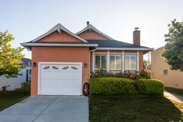 An outside view of a small orange house with a white garage door and well-kept grass lawn that features some shrubs, plants, and flowers.