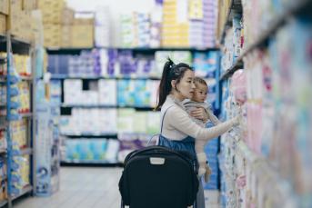 An Asian mother and daughter are selecting baby products at a shopping mall. The mother holds her child in her arms, carefully inspecting the material and quality of the items to choose the most suitable products for her baby.