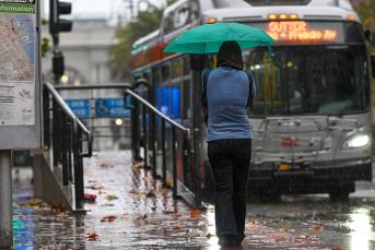 photo of a woman with umbrella waiting at a bus stop during rainy weather