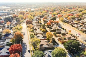 An aerial photo of single-family homes along tree lined streets in a sunny neighborhood