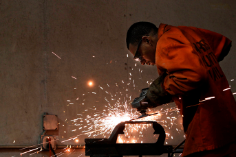 A man wearing an orange jumpsuit uses a tool, sparks fly