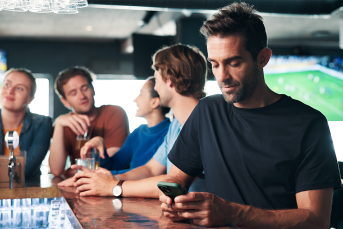 man browsing on smartphone in a pub and sports betting for entertainment