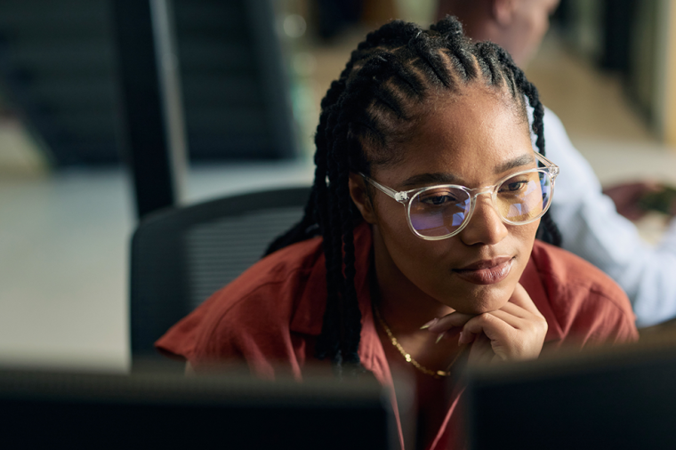 A woman with braids and glasses looks intently at her computer.