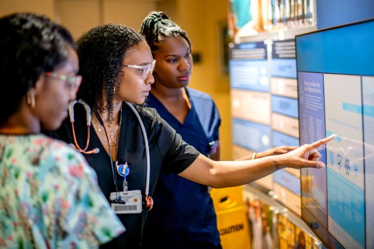 staff review information on a large digital display, with one person pointing to data on the screen.