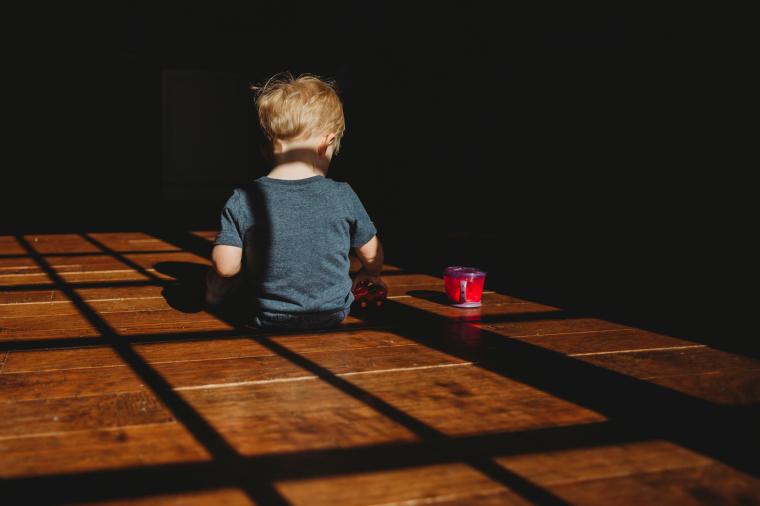 A photo of a toddler sitting in a dark room next to a sippy cup. 