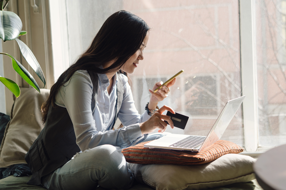 Photo of a young woman holding a credit card and looking at her phone.