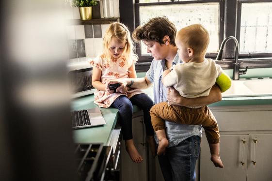 A parent working on a laptop while caring for two children.