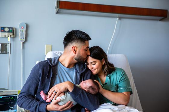 Parents embracing their newborn in a hospital room.
