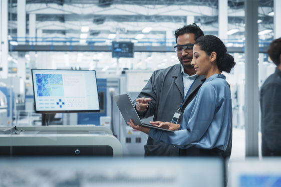 photo of Male Industrial Engineer And Female Supervisor Using Laptop And Talking At An Electronics Factory