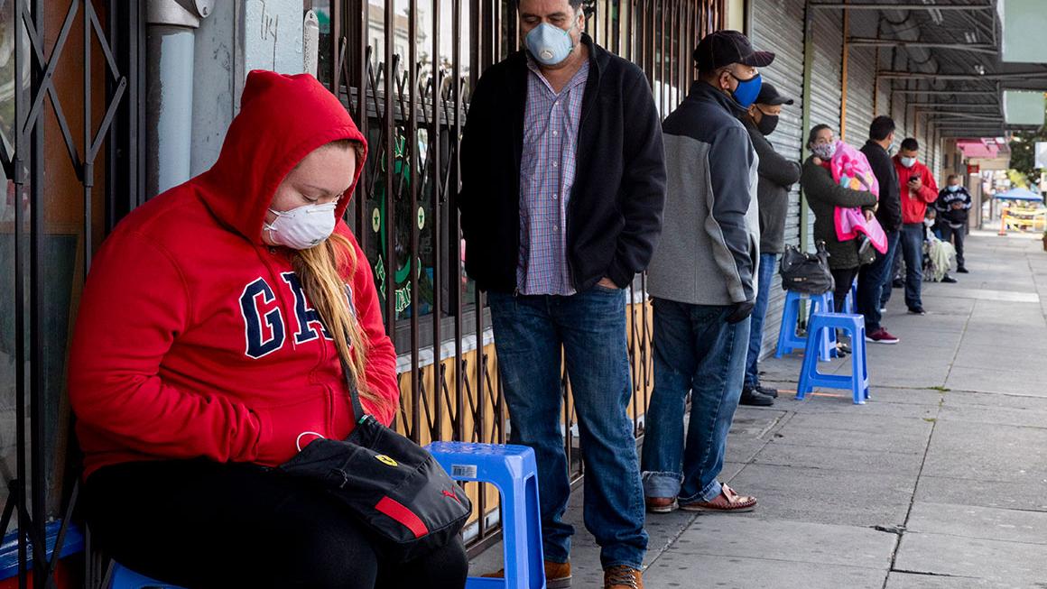 Francisco Montero (center) of Richmond wears a mask while waiting with others in a long line outside of Terra Nova Clinic in the Fruitvale neighborhood of Oakland
