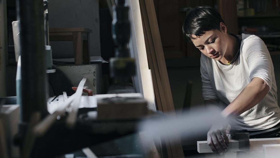 Woman sawing wood in an industrial warehouse.