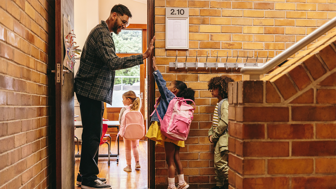 photo of elementary school teacher greeting his students at the door with a high-five