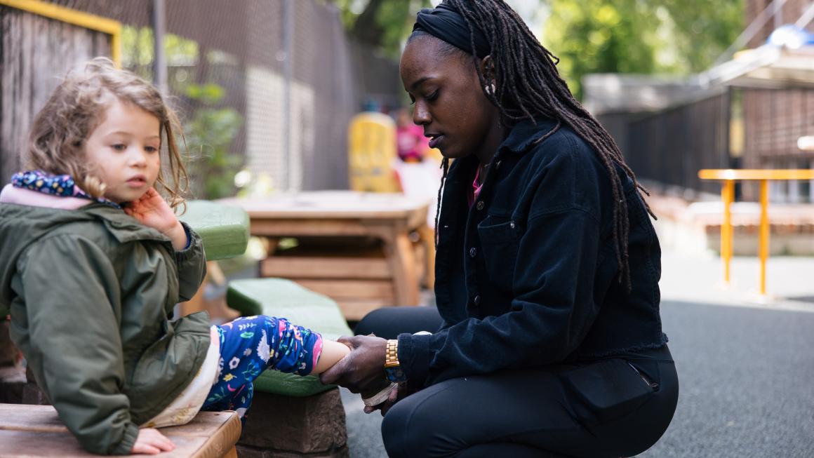 A child care worker squats to put shoes on a child.