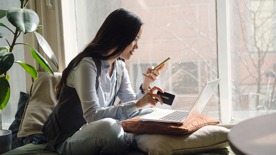 Photo of a young woman holding a credit card and looking at her phone.