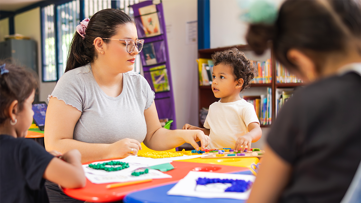 An early childhood teacher plays with educational toys in a kindergarten classroom.