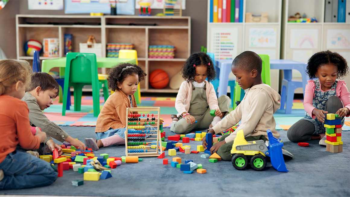 Image of a diverse group of young kids playing with blocks and other toys in a classroom.