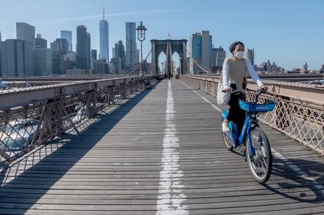Woman wearing mask rides bike across Brooklyn Bridge