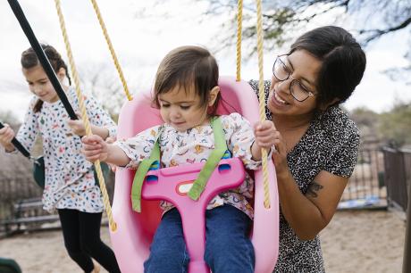 image of child being pushed on swing by caretaker