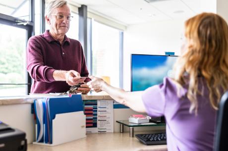 A man reaches forward and hands a card to a receptionist at a doctor's office