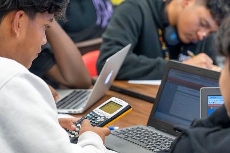 Students using graphing calculcatiors and a laptop while in a classroom