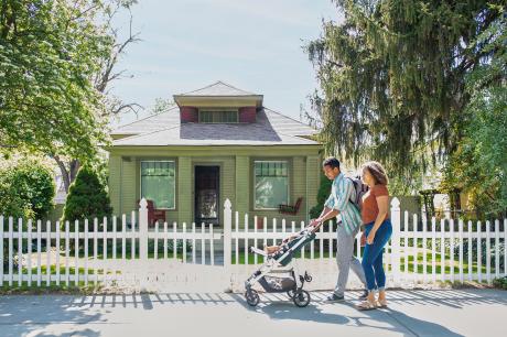 A mother and father pushing a baby in a stroller down a neighborhood sidewalk.