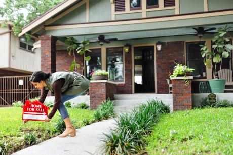 A real estate agent places a for sale sign in front of a home.