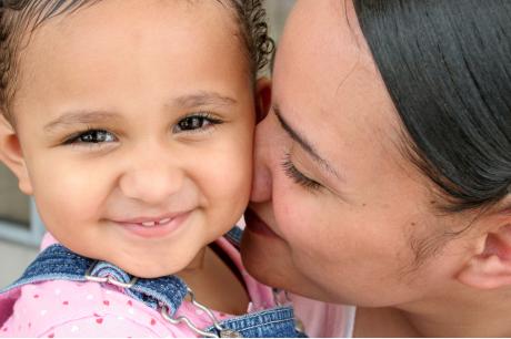 A mother kisses her toddler, who is looking at the camera