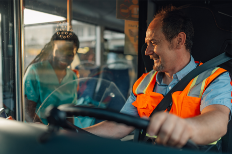 A bus driver smiles while wearing an orange vest 