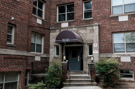 Brick apartment building entrance with steps, railing, shrubs, and awning labeled “5616.”
