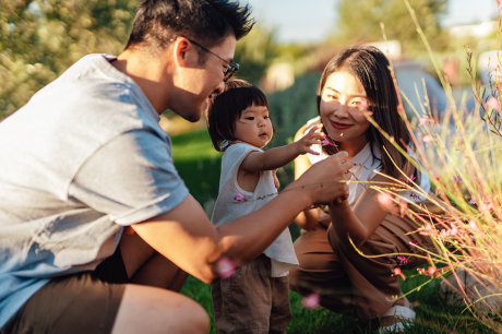 Photo of a young Asian American couple playing with their daughter outside.